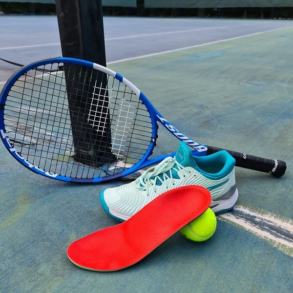 Orthotics for tennis shoes are displayed next to a tennis ball