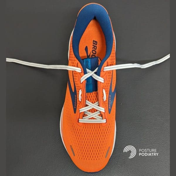 Image displaying orange shoe with shoe lacing designed to decrease pressure on a high instep.